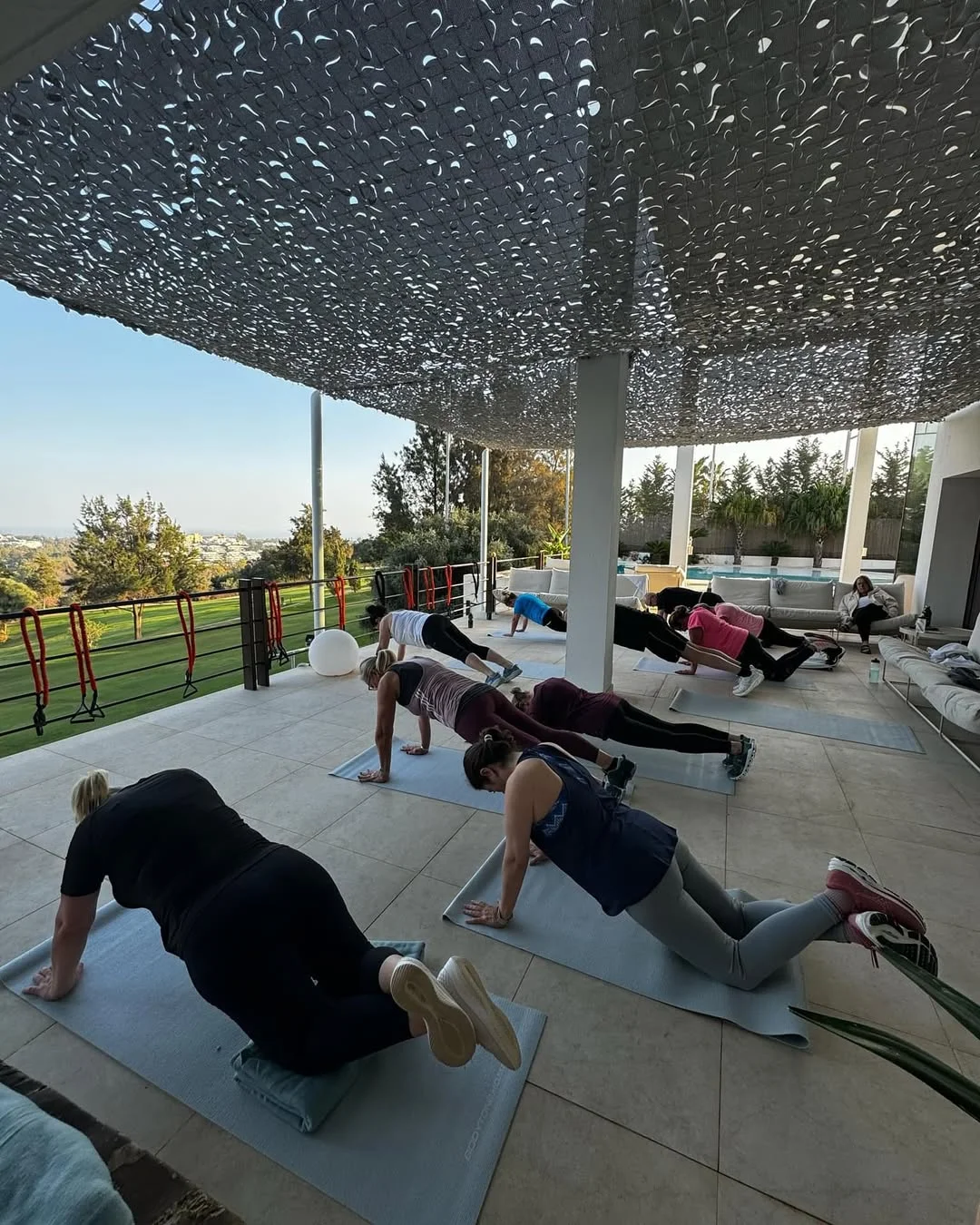 Bootcamp-deltagere laver coretræning på yogamåtter i skyggefuldt udendørsområde
